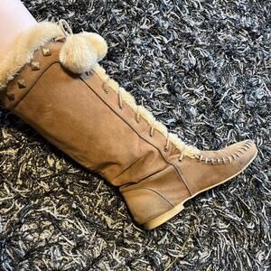 tall, brown, flat-heeled boot, laceup detailing, faux fur lining,studs,pom-poms.